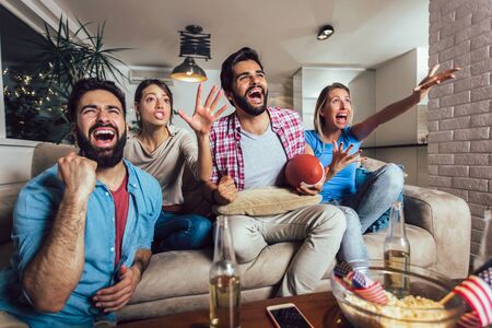 Friends cheering sport league together on tv and celebrating victory at home.Friendship, sports and entertainment concept.の写真素材