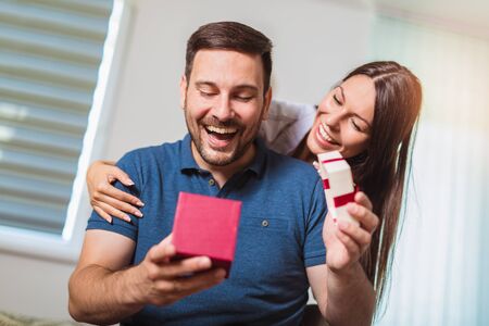 Smiling woman surprises his boyfriend with present at home