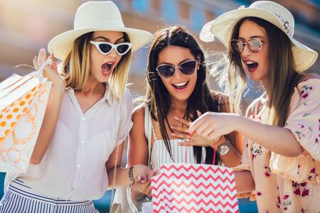 Three beautiful girls in sunglasses with shopping bags in city.の写真素材