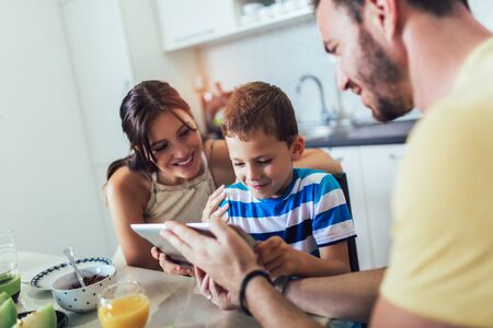 Family eating breakfast at kitchen table and using digital tablet.