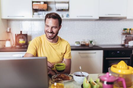 Busy man working at home, using laptop while having breakfast.の写真素材