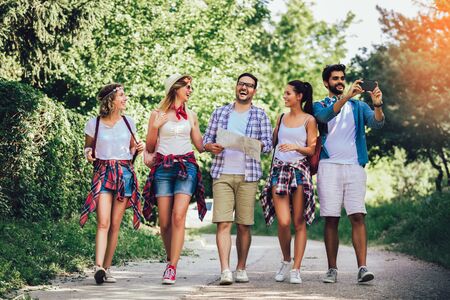 Group of smiling friends walking with backpacks in woods using smart phone - adventure, travel, tourism, hike and people concept. Young Men And Women On Hike Tourists Adventure Activityの写真素材