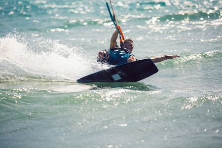 Professional kiter makes the difficult trick on a beautiful background. Kitesurfing Kiteboarding action photos man among waves quickly goesの写真素材