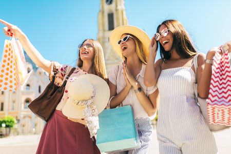 Three beautiful girls in sunglasses with shopping bags in city.の写真素材