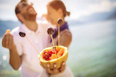 Young couple eating fruit on the beach- summer party with friends and healthy food concept