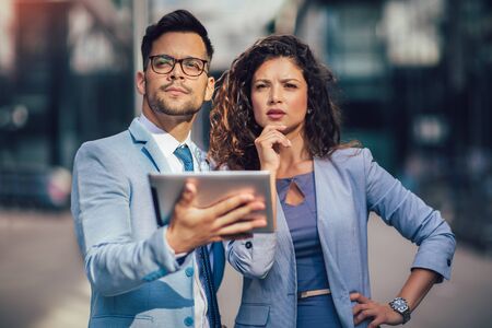 Handsome man and beautiful woman as business partners using digital tablet outdoorの写真素材