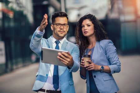 Handsome man and beautiful woman as business partners using digital tablet outdoorの写真素材