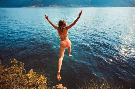 Young woman jumping from a rock into the sea.の写真素材