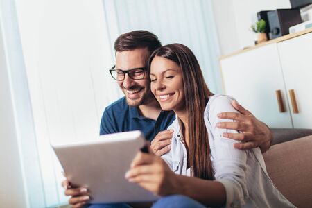 Young couple watching media content online in a tablet in the living room.の写真素材