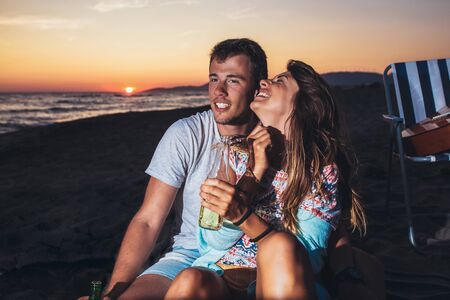 Young couple at the beach having fun, laughing and drinking beerの写真素材