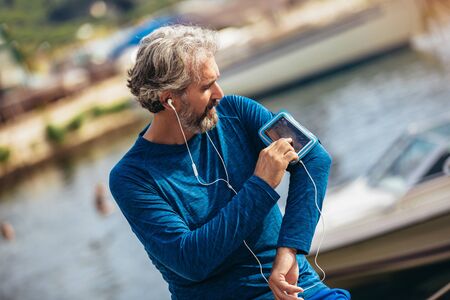 Happy senior athlete listening music over earphones.