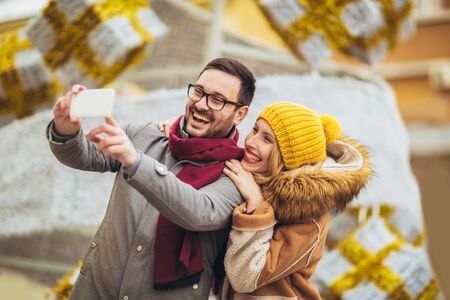 Young beautiful couple with Santa hats make selfie photo in the city.の写真素材