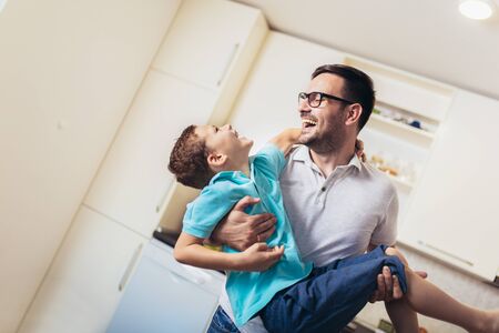 Image of satisfied smiling man piggybacking his son while having fun in modern studio apartmentの写真素材