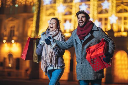 Young couple in the city centre with holiday's brights in background. Man presenting gift to woman.の写真素材