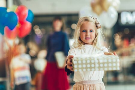 Little girl holding gift in shopping mall, having fun with family.の写真素材