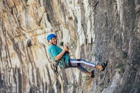 Senior man with a rope climbing on the rock.