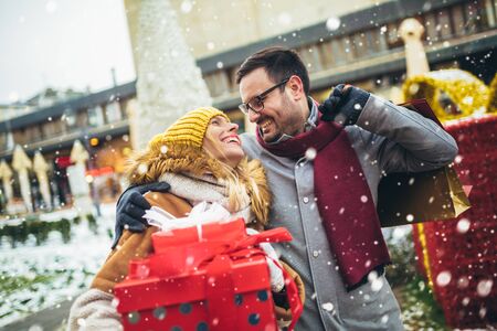 Young couple dressed in winter clothing holding gift boxes outdoor. の写真素材