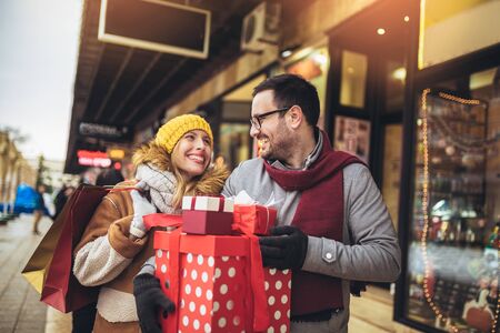 Young couple dressed in winter clothing holding gift boxes outdoor. の写真素材