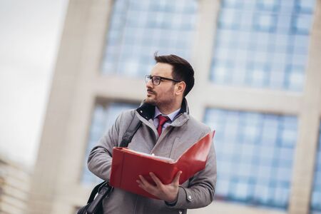 Young attractive businessman holding documents, papers. Young concentrated man reading documents,  outdoors in urban area.の写真素材