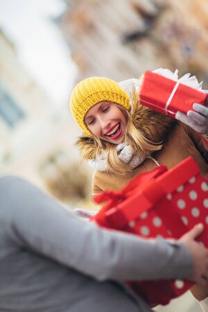 Young couple dressed in winter clothing holding gift boxes outdoor.の写真素材