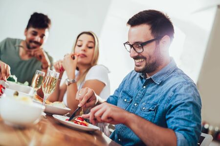 Cheerful young people enjoying meal while sitting at the dinning table on the kitchen together.の写真素材