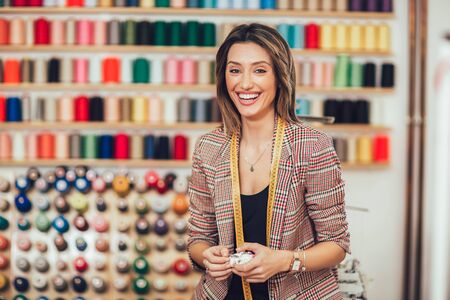 Portrait of happy dressmaker woman in studio. Background of colorful sewing thread.の写真素材