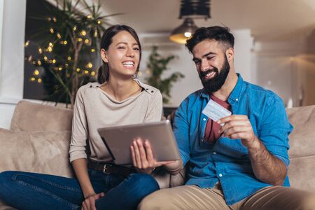 Smiling couple using digital tablet and credit card at homeの写真素材