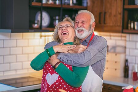 Beautiful senior couple is dancing and smiling while cooking together in kitchenの写真素材