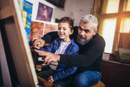 Father and son working and painting together in art studioの写真素材