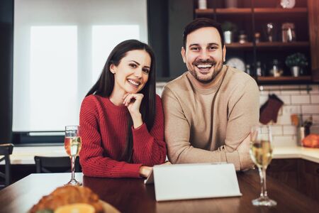 Beautiful young couple is using a digital tablet and smiling while cooking in kitchen at homeの写真素材