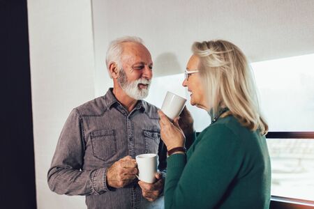 Senior couple holding white mugs at home