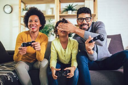 African American family at home sitting in sofa couch and playing console video games together