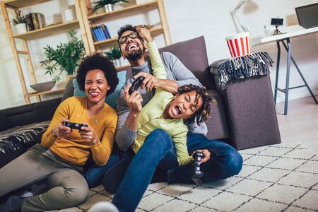 African American family at home sitting in sofa couch and playing console video games together