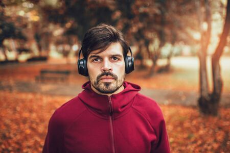 Portrait of  young man on a morning jogging in the autumn park, man listening to music with headphonesの写真素材