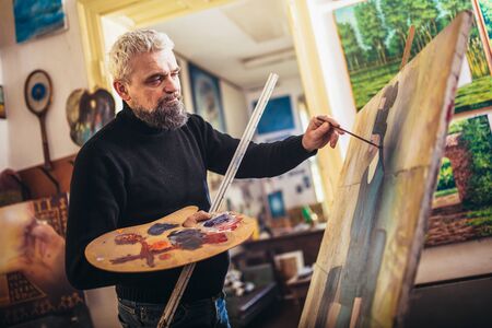 Mature man painting on canvas in art studio.