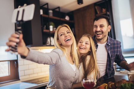 Girl and her beautiful parents are cutting vegetables and smiling while cooking in kitchen at home make selfie photo.の写真素材