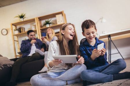 Children sister and brother playing using phone and digital tablet on floor while young parents...