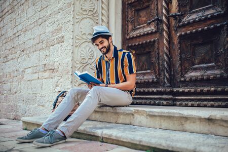 Smiling student reading a book outdoor, studying and preparing for exams at the university or college.の写真素材