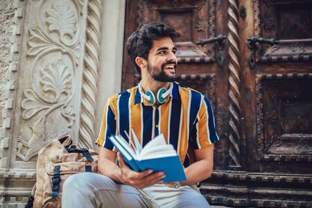 Smiling student reading a book outdoor, studying and preparing for exams at the university or college.の写真素材