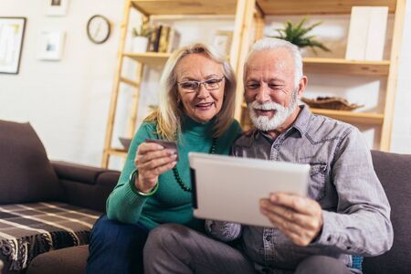 Happy seniors ordering dinner online on laptop, paying with credit card at home. Quarantine.