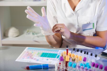 Caucasian female laboratory assistant in white uniform sitting in lab and putting sterile rubber...