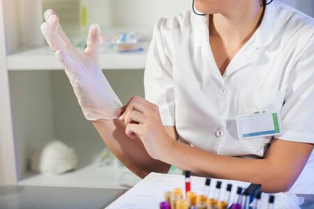 Caucasian female laboratory assistant in white uniform sitting in lab and putting sterile rubber...