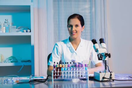 Smiling young female scientist using microscope and looking at camera while working in the...