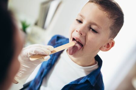 Pediatrician checks the throat of a boy. Tonsillitis, inflammation of the tonsils, child with open mouthの写真素材