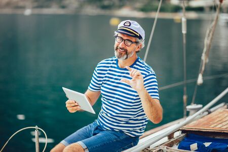 Mature man standing on the deck of his boat and using digital tablet on a sunny afternoon.の写真素材