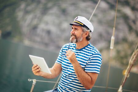 Mature man standing on the deck of his boat and using digital tablet on a sunny afternoon.