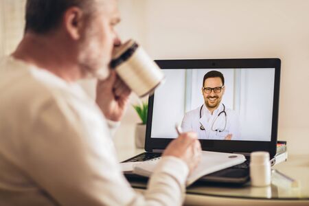 Back view of man making video call with her doctor while staying at home.の写真素材
