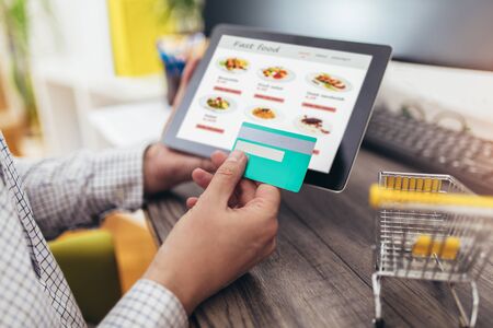 Hands of a man ordering fast food with a digital tablet, paying with credit card.の写真素材