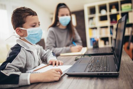 Boy and girl studies at home, wear protective masks, and doing school homework. Distance learning online education.の写真素材