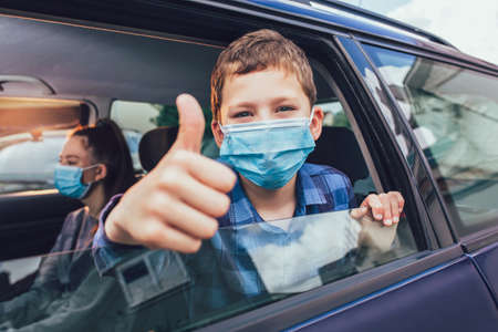 Kids wearing anti virus masks and using digital tablets in the car. Kids are travelling in car during coronavirus outbreakの写真素材